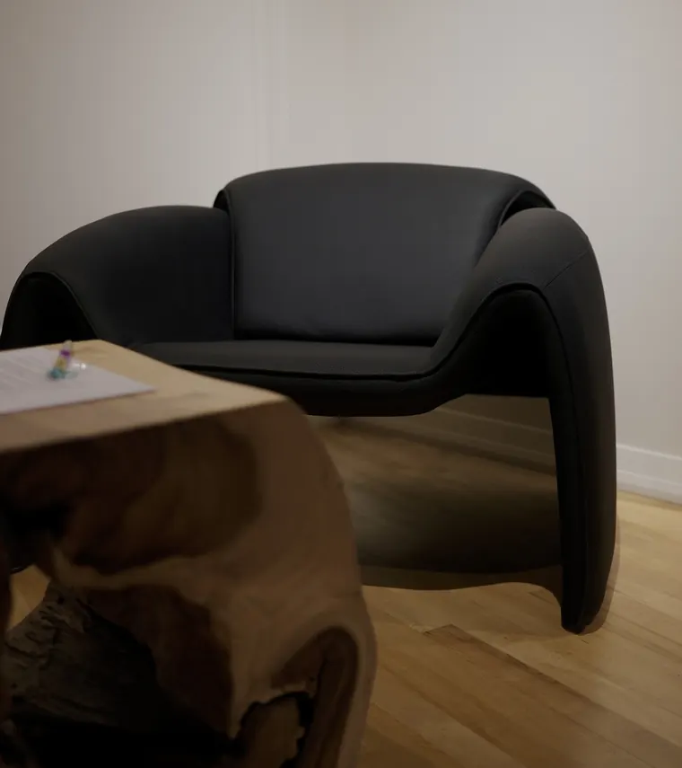 A sculptural black leather armchair beside a carved raw-wood side table in the lounge corner