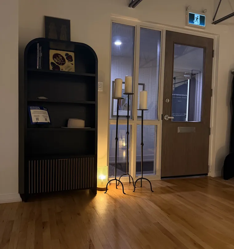 The studio entrance in warm lamplight, with an arched black bookshelf and three tall candles on iron stands