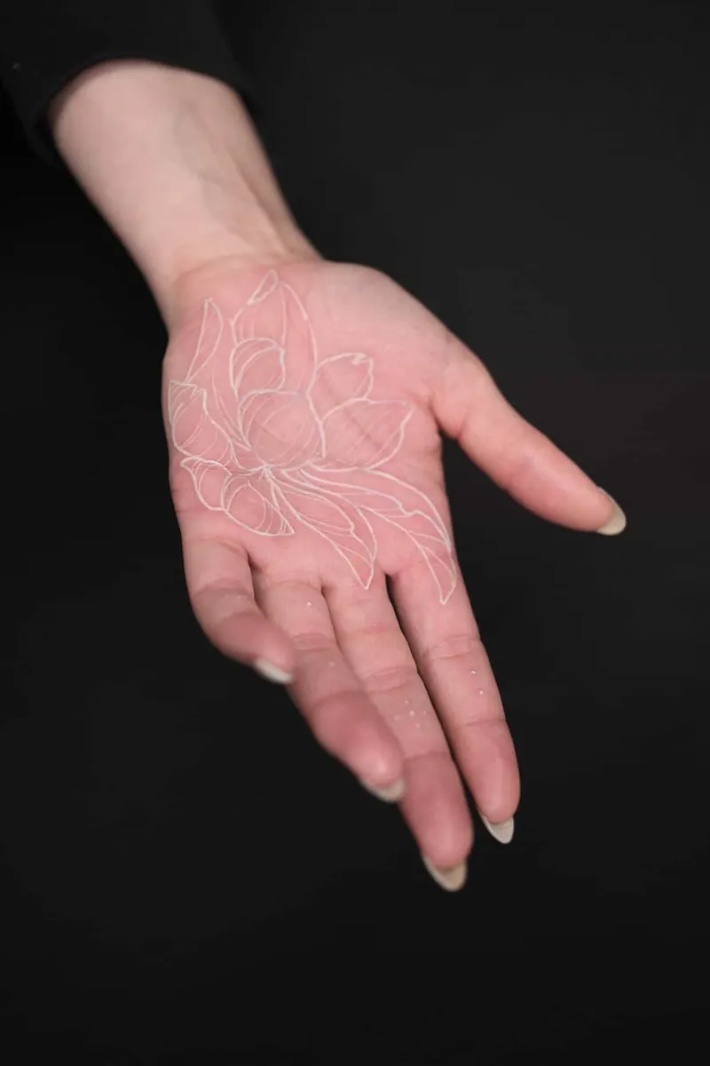 An open palm on a black background with a white-ink outline of a lotus flower