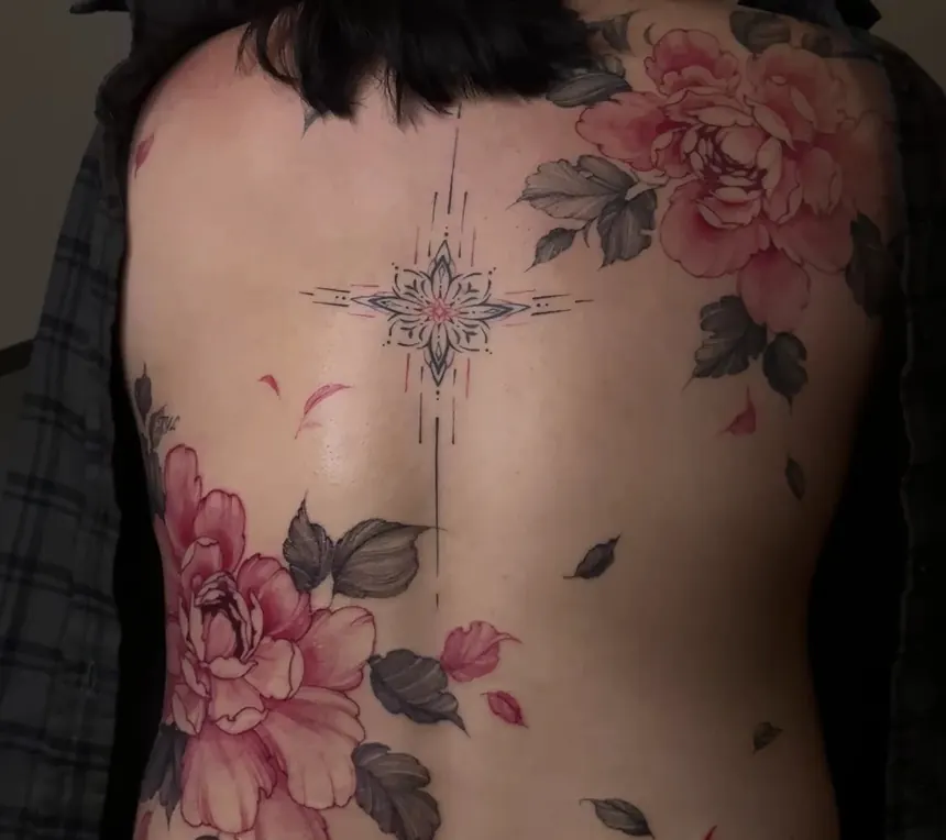 The upper back of a person with dark hair, tattooed with pink-red peonies, black leaves and a fine ornamental star along the spine